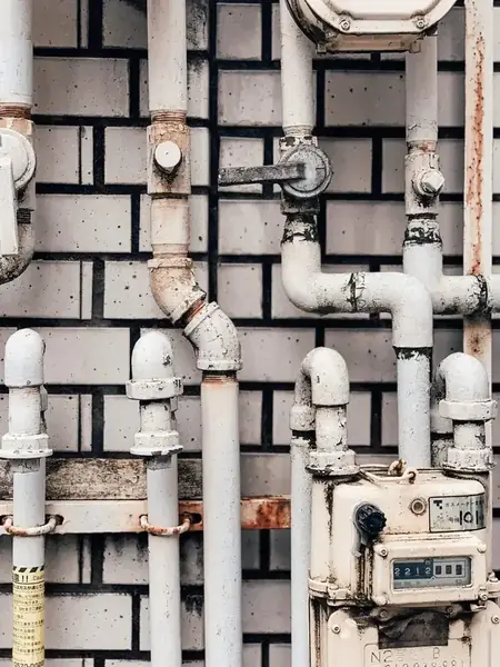 White painted pipes and gas meter on a brick wall