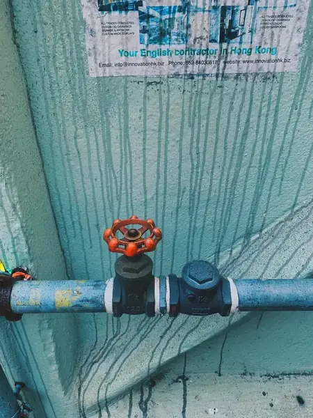 Red valve on a blue water pipe against a weathered wall
